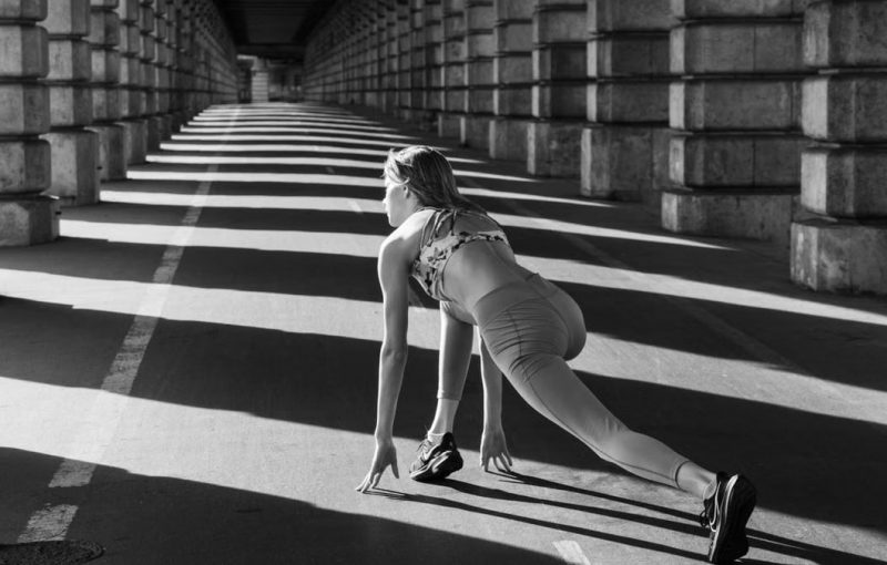 Woman stretching under urban bridge in monochrome capturing dynamic sport pose.